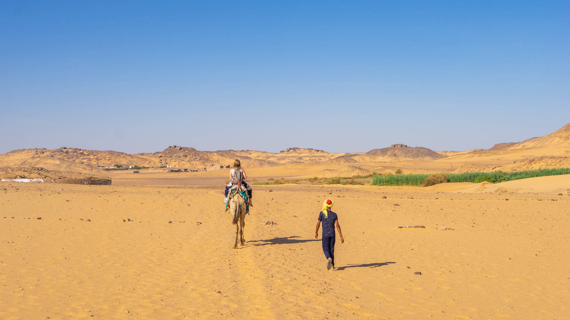 Dame rijdend op een kameel tijdens de kamelentocht in de woestijn van Aswan onder begeleiding van een lokale Egyptenaar